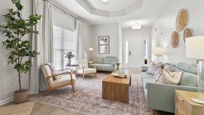 Ein geräumiges Wohnzimmer mit einer Couch, Sesseln, einem Couchtisch und einer Topfpflanze.