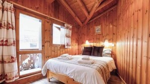 A wooden cabin room with a bed, a window with curtains, and a lamp. - 4-bedroom chalet with jacuzzi and sauna (La Plagne Tarentaise)