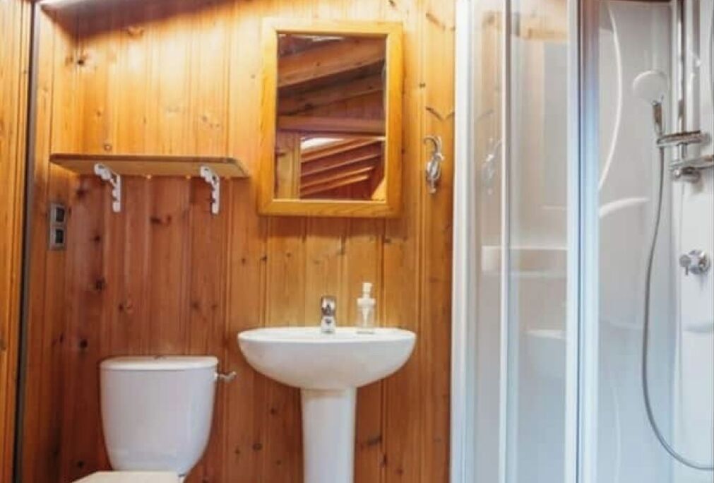 Un baño con paneles de madera, un inodoro, un lavamanos pedestal y una cabina de ducha.