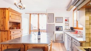 A kitchen with wooden cabinets, a central island, a chandelier, and a view to the outside. - 4-bedroom chalet with jacuzzi and sauna (La Plagne Tarentaise)