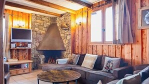 A cozy living room with a stone fireplace, wooden walls, and a comfortable sofa. - 4-bedroom chalet with jacuzzi and sauna (La Plagne Tarentaise)