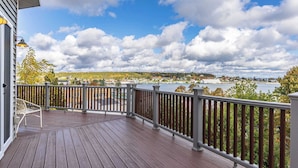A wooden deck with a railing, overlooking a body of water and distant land.