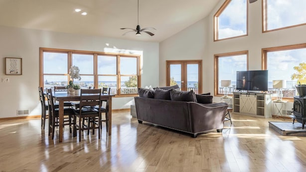 A spacious living area with a dining table, sofa, and TV, large windows with a view, and a ceiling fan.