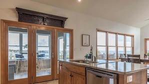 A kitchen with wooden cabinets, a stainless steel dishwasher, and large windows offering a view of the sea.