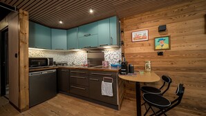 A compact kitchen with teal cabinets, a stainless steel refrigerator, and a wooden dining table with two chairs. - Beautifully renovated studio apartment, sleeps 4, mountain view (Allos)