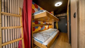 A compact, multi-level bunk bed room with a wooden floor, a colorful geometric wall design, and a door with a handle. - Beautifully renovated studio apartment, sleeps 4, mountain view (Allos)