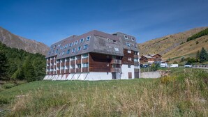 A modern multi-story hotel with a mix of wood and stone facade, located in a mountainous area with a clear sky. - Beautifully renovated studio apartment, sleeps 4, mountain view (Allos)