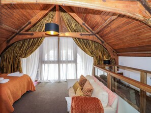 A cozy room with a sloped ceiling, a bed, a sofa, and a large window with curtains.