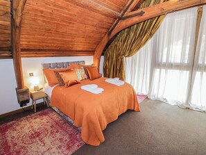 A bedroom with a wooden ceiling, a bed with an orange bedspread, a nightstand with a lamp, and a red patterned rug. - Diamond Lodge (Stafford)