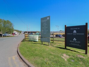 A roadside sign for a seasonal plant center with opening times and a welcome sign for Great Haywood Marina.