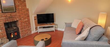 A cozy living room with a brick fireplace, a flat-screen TV, grey sofas, and a wooden coffee table.