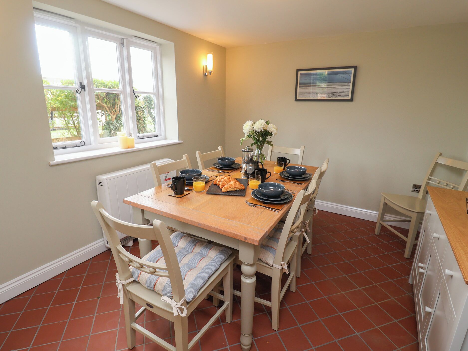 A dining area with a wooden table, chairs, and a window with a view of greenery.