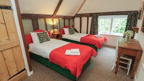 A room with two beds, each with red and green bedding, a wooden desk, and a window with curtains.