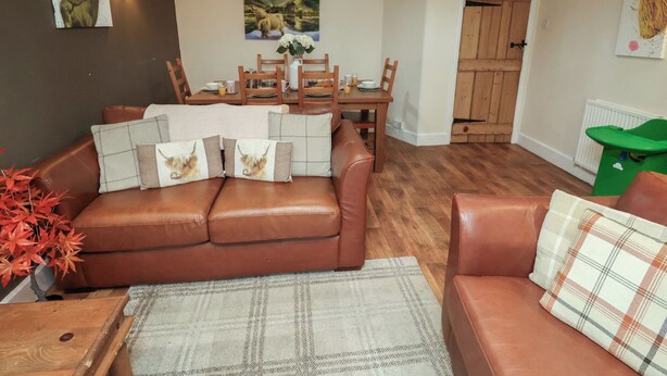 A cozy living room with a brown leather sofa, a dining table with chairs, and a wooden door.