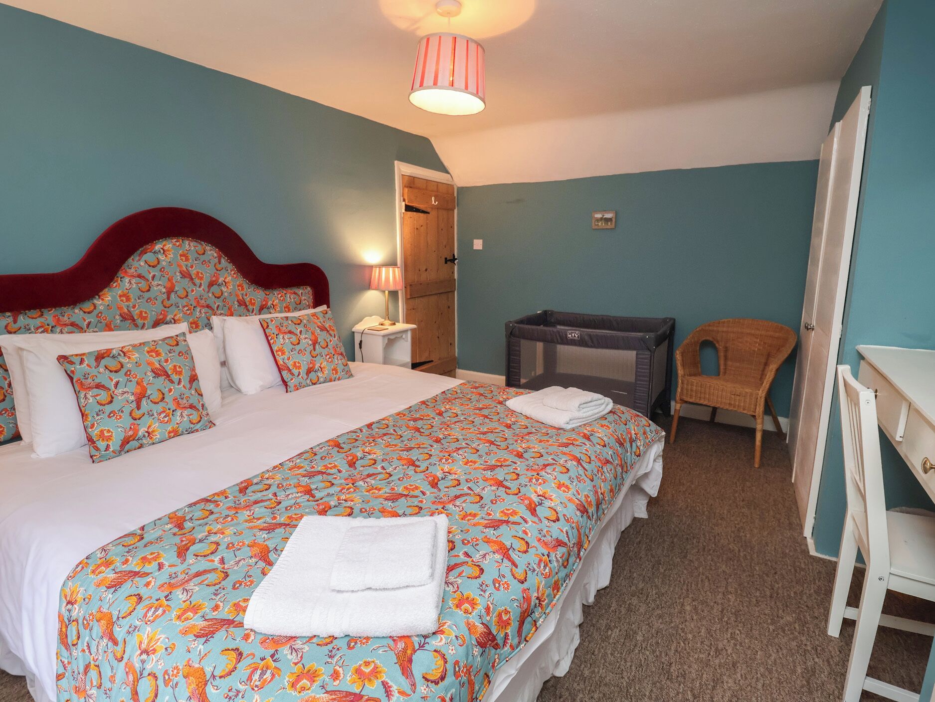 Ein Schlafzimmer mit einem Bett, einem Nachttisch, einem Stuhl, einem Schreibtisch und einem Babyreisebett.