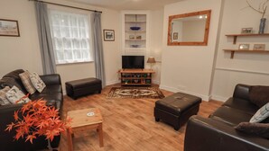 Un salon avec un canapé en cuir foncé, une table basse en bois, un téléviseur posé sur un meuble et un grand miroir accroché au mur.