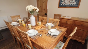 Une table de salle à manger en bois, mise avec des assiettes, des bols, des couverts et un vase de fleurs.