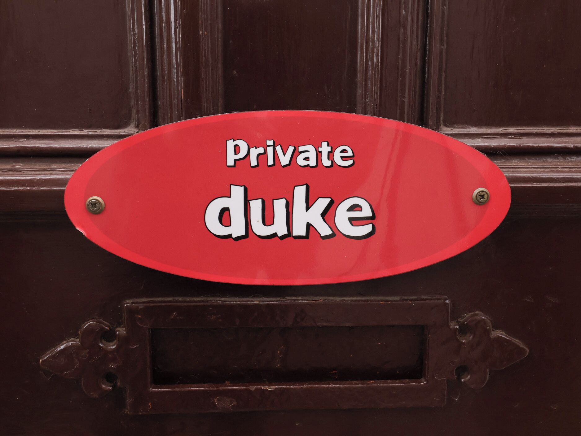 A red oval sign with the words 'Private duke' on a dark wooden door.