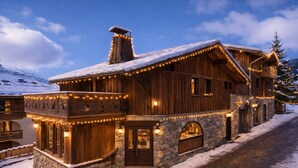 Une cabane en bois aux murs de pierre, avec un toit enneigé et des guirlandes lumineuses.