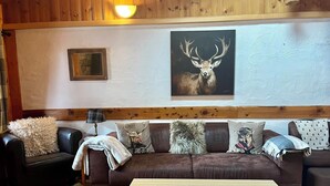 Un salon avec un canapé en cuir marron, une table basse en bois et une décoration murale sur le thème des cerfs.