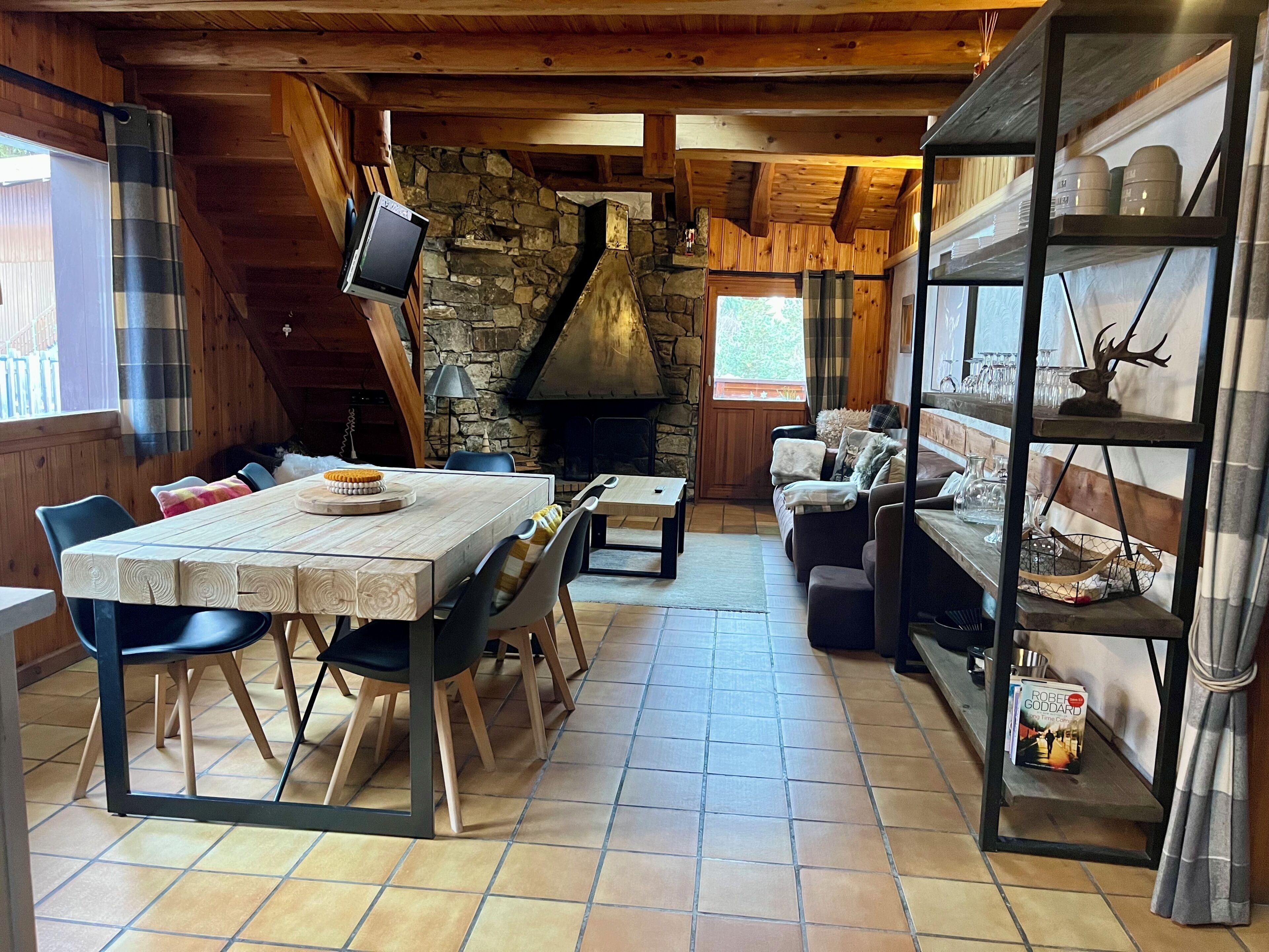 A cozy cabin interior with a stone fireplace, wooden furniture, and a bookshelf.
