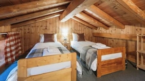 Une chambre confortable située dans les combles, avec des poutres en bois, deux lits et un rideau à carreaux.