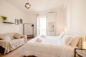 Een slaapkamer met een bed, een bank, een nachtkastje, een lamp, een spiegel en een raam.