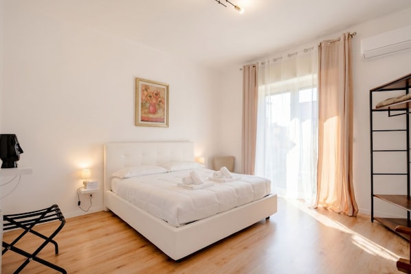 A bedroom with a bed, bedside lamps, a desk, a chair, a bunk bed, and a painting on the wall.
