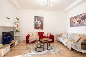 A modern living room with a red sofa, grey sofa, a TV, a world map, and a painting of a character.