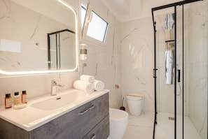 A modern bathroom with a large mirror, a white sink, a shower enclosure, and a toilet.