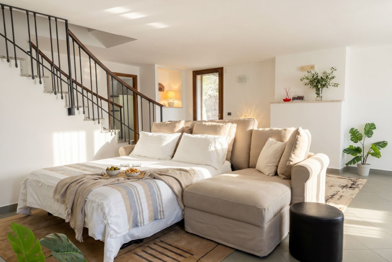 Un dormitorio con una cama, un sofá, un reposapiés negro, una escalera y una planta en maceta.