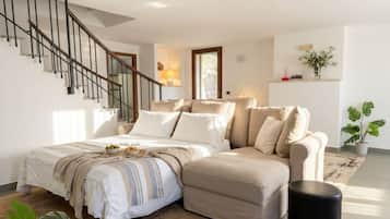 Un dormitorio con una cama, un sofá, un reposapiés negro, una escalera y una planta en maceta.