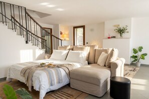 A bedroom with a bed, a sofa, a black ottoman, a staircase, and a potted plant.