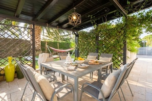 An outdoor patio with a table set for dining, surrounded by chairs, a hammock, and potted plants.