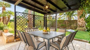 An outdoor patio with a table and chairs, surrounded by a fence, and a view of a garden.