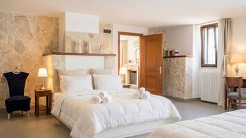 A bedroom with a stone wall, a bed with white bedding, a chair, a lamp, and a wooden door.