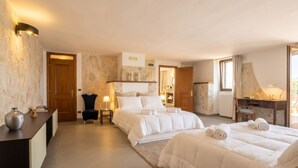 A hotel room with a large bed, a desk, a chair, a small table, and a lamp.