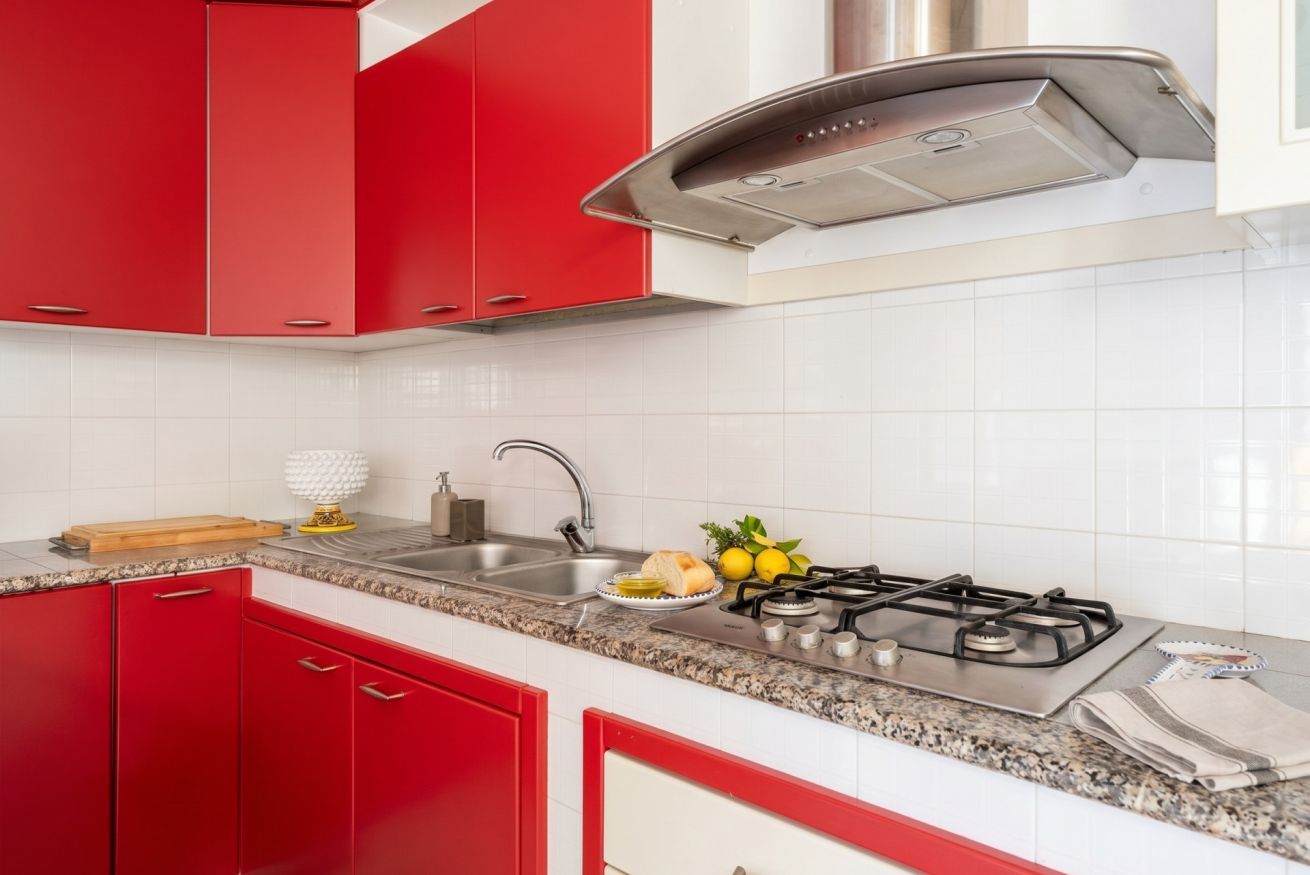 Een keuken met rode kasten, een roestvrijstalen afzuigkap, een spoelbak, een gasfornuis en een granieten aanrecht.