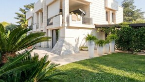 A modern two-story house with a balcony, a stone base, and potted plants.