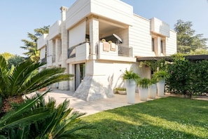 A modern two-story house with a balcony, a stone base, and potted plants.