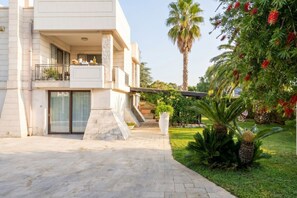 Un bâtiment moderne à deux étages, doté d’un balcon, d’une entrée pavée et de plantes tropicales.