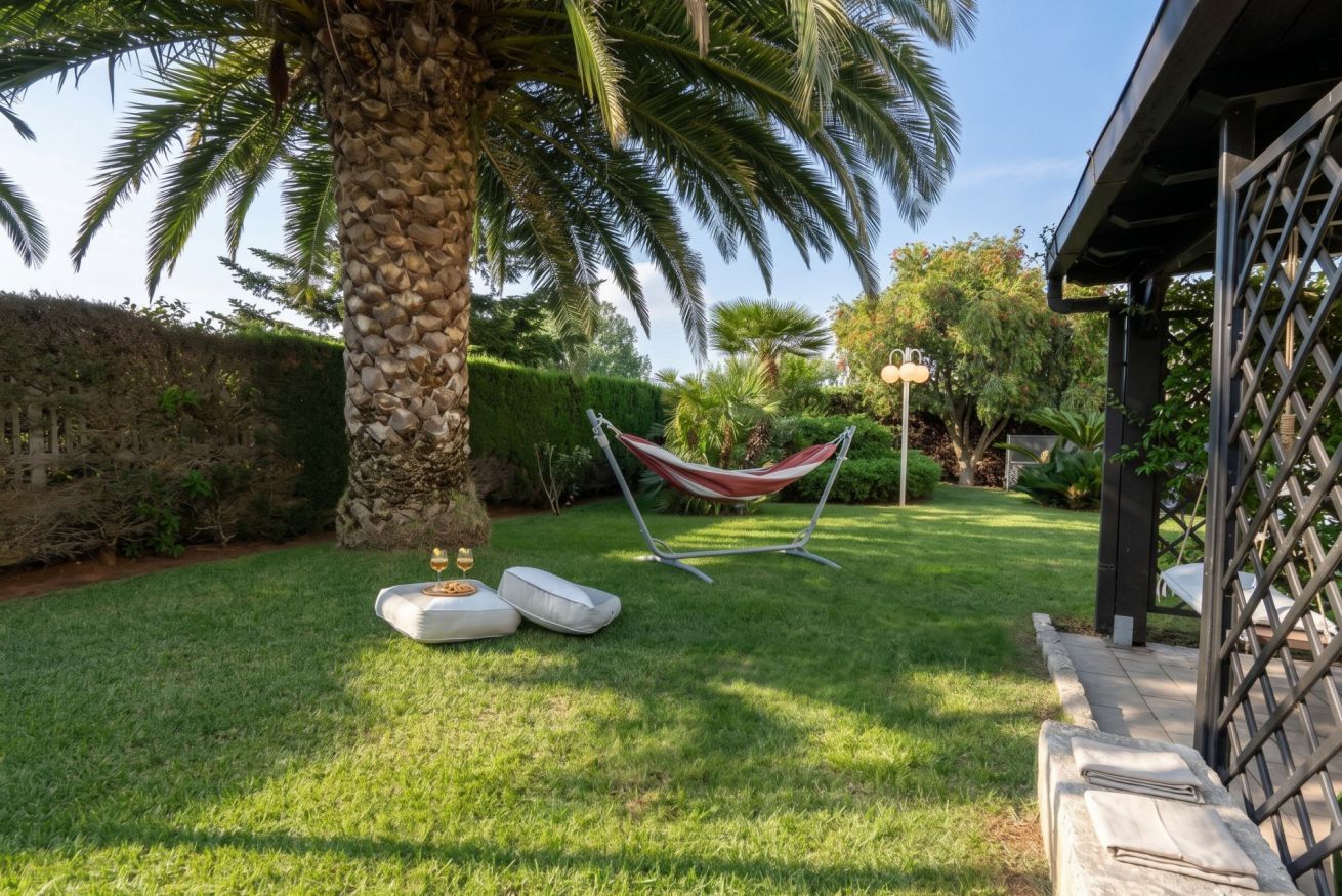 Un jardín bien cuidado con una hamaca, cojines y una palmera.