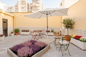 An outdoor patio with a table, chairs, an umbrella, potted plants, and a flower bed. - Covi del Viaggiatore 2 – Modern Comfort, Timeless Charm (Bari)