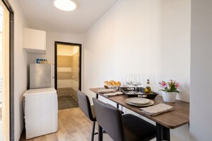 A compact kitchen with a refrigerator, a dining table set with plates, glasses, and a flower vase. - Covi del Viaggiatore 2 – Modern Comfort, Timeless Charm (Bari)