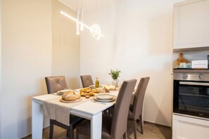 A modern dining area with a table set for four, a chandelier, and a kitchen with an oven.
