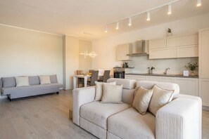 Una sala de estar moderna con un sofá, una zona de comedor y una cocina con armarios blancos.