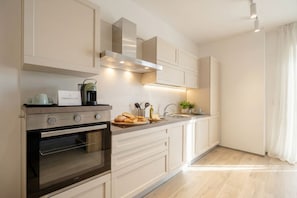 Een moderne keuken met een ingebouwde oven, een roestvrijstalen afzuigkap en een aanrecht met een waterkoker en brood.