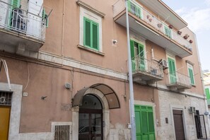 A multi-story building with balconies, a visible entrance, and a street-level window.