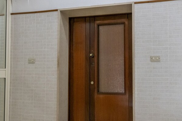 A wooden door with a metal handle and a textured glass panel, set in a room with white tiled walls and a wooden trim.