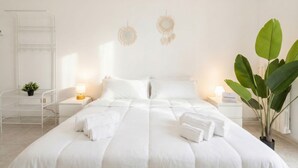 A neatly made bed with white linens, two bedside lamps, a small plant, and a wall-mounted shelf.